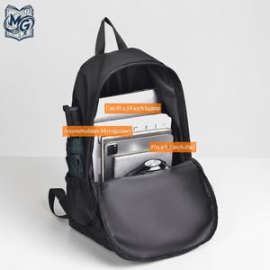 Puede incluir: Una mochila negra con un compartimento principal abierto que contiene una laptop de 14 pulgadas, revistas A4 y un iPad de 9.7 pulgadas. La bolsa tiene un bolsillo lateral con un paraguas verde oscuro y etiquetas de texto sobre capacidad.