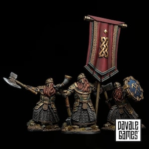 Peut inclure: Trois figurines miniatures de nains avec une armure en cotte de mailles détaillée, des casques et de longues barbes. L'un tient une hache et un cor, l'un porte une grande bannière rouge avec un nœud doré, et l'un tient une hache et un bouclier bleu.