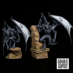 Op de afbeelding: Twee donkergrijze, gevleugelde demonenminiaturen met hoorns en scherpe tanden, elk zittend op een beige, rotsachtige stenen basis met kleine plukjes groen gras. De tekst Pavale Games staat in het zwart op een wit vierkant rechtsonder.