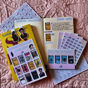 May include: A collection of stationery items including a journal with the text Hudson Williams Book Club, several sticker sheets featuring book covers and character illustrations, and a yellow book. The journal pages contain handwritten notes.