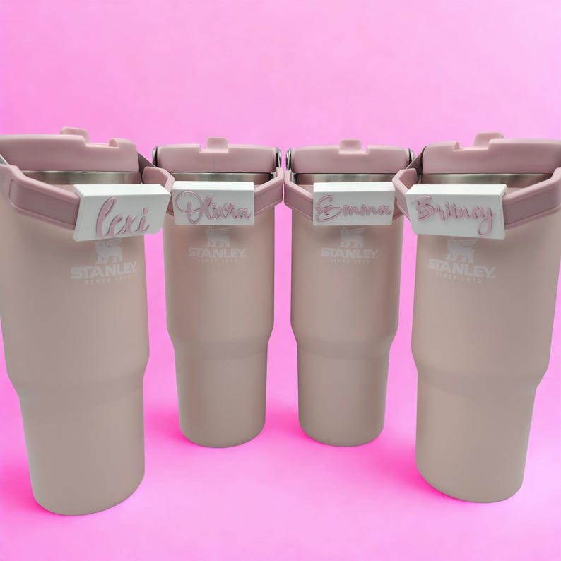 Four personalized pink tumblers with custom 3D printed handle name tags in different names and colors.