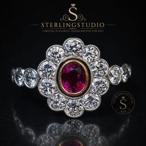 Peut inclure: Une bague en argent avec une pierre centrale ovale rouge foncé sertie dans un chaton doré, entourée d'une auréole de dix pierres claires rondes. L'anneau est orné de pierres claires rondes supplémentaires sur les côtés.