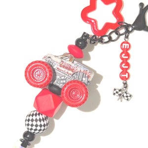 May include: A keychain featuring a miniature monster truck with red wheels, a red star-shaped clasp, and a black chain. It includes red beads spelling EJJT, a checkered flag charm, a large red geometric bead, and a black and white checkered bead.