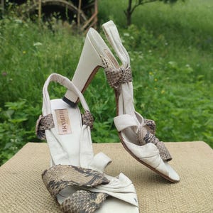 Könnte beinhalten: Ein Paar cremeweiße Slingback-Sandalen mit Blockabsatz, ausgestattet mit Riemen aus Leder mit Schlangenledermuster über dem Vorderfuß und Knöchel. Die Innensohle trägt den Schriftzug BELTRAMI. Das Design umfasst ein gerafftes Lederdetail vorne.