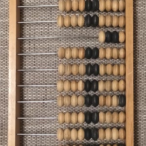 Könnte beinhalten: Ein hölzerner Abakus mit einem rechteckigen Rahmen und zehn horizontalen Metallstäben. Jeder Stab enthält eine Reihe von hellbraunen und schwarzen Perlen, die auf dem Draht verschoben werden können. Die Perlen sind in verschiedenen Mustern angeordnet.