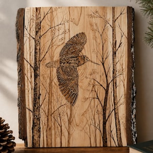 Puede incluir: Una pieza rectangular de madera de color claro con bordes de corteza oscura natural que presenta una ilustración detallada pirograbada de un ave en vuelo centrada entre dos árboles altos y delgados con ramas desnudas y pequeños brotes.