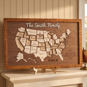 Könnte beinhalten: Ein rechteckiges Wandbild aus Holz mit einer lasergeschnittenen Karte der Vereinigten Staaten und einzelnen Bundesstaaten. Der Text "The Smith Family" steht oben, "USA TRAVEL MAP ADVENTURE AWAITS" unten. Rechts befindet sich eine Windrose.