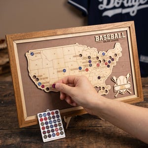 May include: A framed wooden map of the United States featuring a laser-cut design of Major League Baseball stadiums. The map includes text reading BASEBALL MAJOR LEAGUE and TERRY'S STADIUM MAP, accompanied by a sheet of small circular coloured markers.