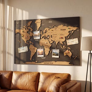 May include: A large rectangular wall-mounted world map featuring laser-cut wooden continents in a light tan finish against a dark charcoal background. The map includes various coloured push pins, four attached photographs, and two airline boarding passes.