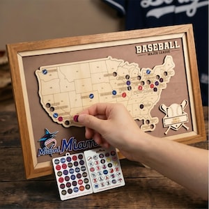 Puede incluir: Un mapa de madera enmarcado de los Estados Unidos con recortes para estadios de béisbol. El mapa incluye el texto BASEBALL MAJOR LEAGUE y un logotipo de los Miami Marlins. Se incluyen dos hojas de pegatinas circulares de equipos.