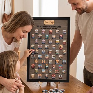Puede incluir: Un tablero de madera enmarcado titulado 50 States Adventure of the United States con una placa personalizada con el nombre David & Evelyn. El tablero presenta una cuadrícula de cincuenta marcadores magnéticos hexagonales con ilustraciones.