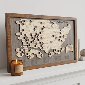 May include: A rectangular wooden wall map of the United States featuring cutouts for National Parks, mounted on a grey wood-grain background within a brown frame. The map includes engraved park names, small animal icons, and a custom plaque.