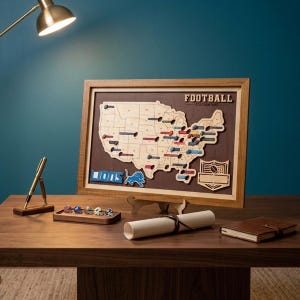 May include: A framed wooden map of the United States featuring the text FOOTBALL STADIUM MAP, a Lions logo, and small football helmet markers placed on various states. The display includes a wooden pen stand, a scroll, and a small leather notebook.
