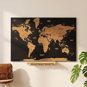 May include: A rectangular wall-mounted world map featuring tan-coloured wooden continents set against a solid black background. The map includes labels for major countries and oceans, with several colourful push pins inserted into various locations.