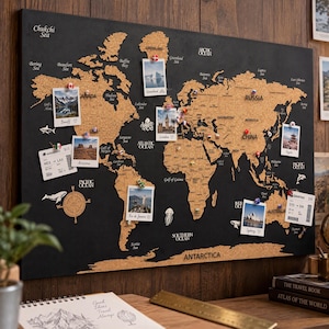 May include: A rectangular world map wall board featuring cork continents set against a black background. The map includes printed geographical labels, small decorative sea creature illustrations, and several pinned photographs and travel boarding passes.