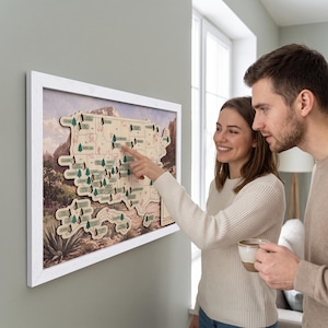 Pode incluir: Um mapa de parede emoldurado dos Estados Unidos com um design de madeira em camadas e pequenos ícones de árvores verdes marcando vários parques nacionais. O mapa está sobre um fundo de paisagem e tem uma moldura branca simples.