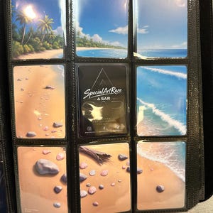 May include: A black binder with clear plastic pockets containing nine rectangular cards. Eight cards feature beach and ocean scenes with sand, shells, and blue water. One central black card displays the white text Special Art Rare A SAR.