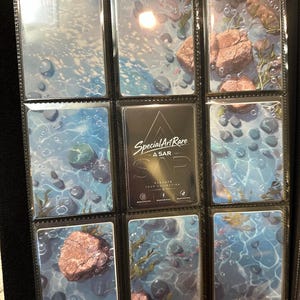 May include: A black trading card binder page containing nine rectangular cards. Eight cards feature a blue water scene with rocks and bubbles. The centre card is black with white text reading Special Art Rare A SAR Elevate Your Collection.