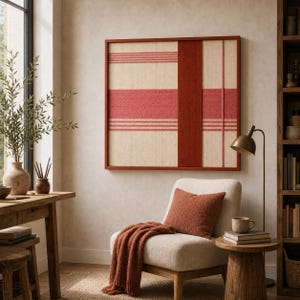 May include: A framed wall art piece with a woven design in cream, red, and brown tones. The artwork features horizontal and vertical stripes, creating a geometric pattern. The frame is a dark reddish-brown color.