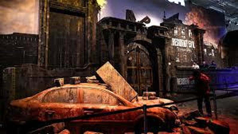 Peut inclure: Sc&egrave;ne d&eacute;taill&eacute;e d'une exposition Resident Evil avec une voiture orange rouill&eacute;e au pare-brise bris&eacute; devant un grand b&acirc;timent us&eacute;. Le b&acirc;timent a une grande porte arqu&eacute;e et les mots "RESIDENT EVIL" sont visibles.