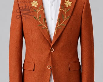 May include: A burnt orange blazer featuring gold floral embroidery on the lapels, two front buttons, and a white collared shirt underneath. The text CROWNCUT BESPOKE with a crown and scissors icon is visible on the upper left side of the blazer.