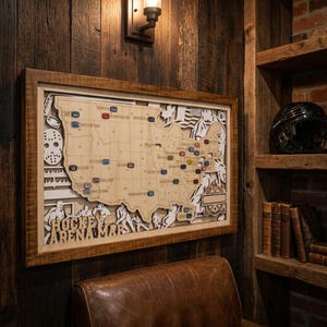 May include: A rectangular wooden wall art piece featuring a layered map of the United States with hockey-themed cutouts, including a goalie mask and players. The map displays various coloured markers and the text HOCKEY ARENA MAP in wood.
