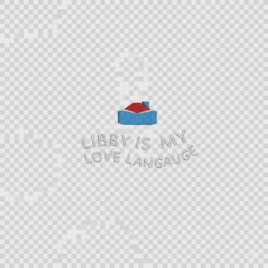 May include: An embroidered design featuring a small house icon with a red roof and blue walls, positioned above the text "LIBBY IS MY LOVE LANGAUGE" stitched in a light grey thread. The design is presented against a transparent background.