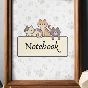 Puede incluir: Un cuaderno enmarcado con un fondo claro cubierto de huellas de patas. El cuaderno presenta una pancarta color crema con la palabra "Notebook" en escritura negra. Encima de la pancarta hay tres gatos de dibujos animados de varios colores.