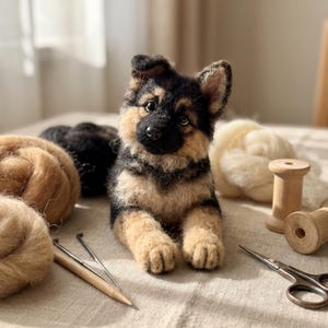 Könnte beinhalten: Eine nadelgefilzte Welpenfigur eines Deutschen Schäferhundes aus schwarzen und lohfarbenen Wollfasern mit dunklen Augen und schwarzer Nase. Der Welpe liegt in einer liegenden Position mit geneigtem Kopf, umgeben von loser Wolle, Holzspulen und Werkzeugen.