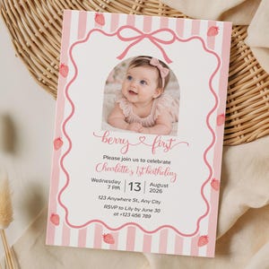 Puede incluir: Una tarjeta de invitación de cumpleaños rectangular con fondo de rayas rosas y blancas e ilustraciones de fresas. El centro muestra la foto de un bebé en un marco arqueado, con el texto: berry first, Charlotte's 1st birthday, Wednesday August 13 2026.