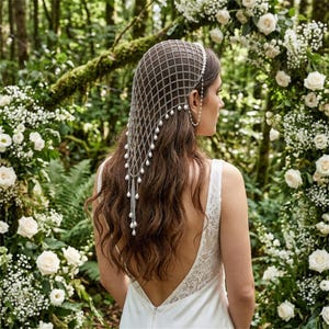 May include: A silver-toned chain mail headpiece featuring a diamond-shaped grid pattern adorned with small white faux pearls hanging from the intersections and edges, draping over the back of the head and hair in a cascading, layered design.
