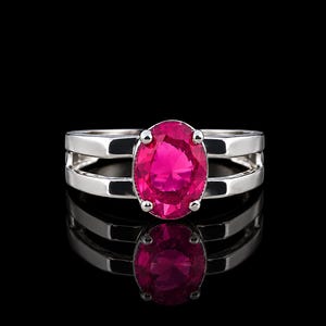 Peut inclure: Une bague argentée ornée d'une grande pierre précieuse rose vif de taille ovale, fixée par quatre griffes. L'anneau présente un design à double branche, formant deux barres parallèles qui se rejoignent au niveau du sertissage central.