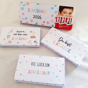 May include: Four rectangular white boxes decorated with colorful pastel polka dots. The boxes feature German text including "SCHULKIND 2026," "hurra, ich bin ein SCHULKIND," "Du bist 1.KLASSE," and "VIEL GLÜCK ZUM SCHULSTART," along with small school-themed icons.
