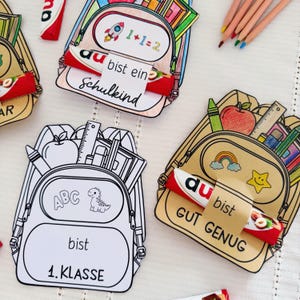 Op de afbeelding: Papieren rugzak-uitsparingen met schoolspullen zoals appels, linialen en kleurpotloden. Sommige zijn ingekleurd, andere zijn zwart-wit omtrekken. Elke rugzak heeft een papieren band met een chocoladereep met Duitse tekst zoals bist ein Schulkind.