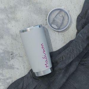 Peut inclure: Un gobelet en acier inoxydable gris clair mat avec le texte "Maison" écrit en écriture magenta verticale sur le côté. Le gobelet présente un bord argenté à la base et au sommet, accompagné d'un couvercle en plastique transparent amovible.