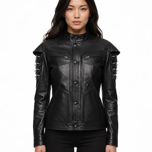 May include: A black leather jacket featuring a mandarin collar, a front button closure, and two horizontal zippered chest pockets. The shoulders and upper sleeves are accented with layered, tiered panels and metallic hardware details.