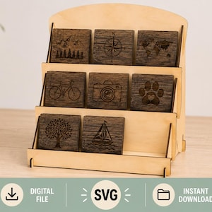 May include: A light-colored wooden tiered display stand holding eight square dark wood coasters. Each coaster features a unique laser-engraved design, including a mountain range, compass, world map, bicycle, camera, paw print, tree, and sailboat.
