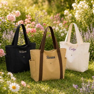 Pode incluir: Três sacolas de lona nas cores preta, bege e branco off-white, cada uma com dois bolsos laterais, alças duplas e um bolso frontal com botão de pressão. As bolsas são bordadas com os nomes Willow, Sienna e Evelyn em fonte cursiva.