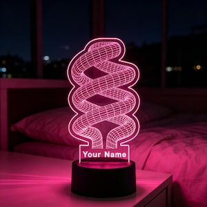 May include: A custom LED lamp featuring a glowing pink 3D wireframe spiral design on a flat acrylic panel. The base is black and cylindrical, and the acrylic panel includes the printed text Your Name at the bottom, illuminated in bright pink light.