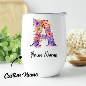 Könnte beinhalten: Ein weißer Becher mit einem großen Buchstaben A, der mit bunten Blumen und einem lila Schmetterling verziert ist. Unter dem Buchstaben steht der Text Your Name in schwarzer Schrift. Ein Pfeil zeigt auf den Text mit der Beschriftung Custom Name.