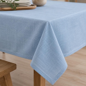 May include: A light blue tablecloth with a visible woven texture draped over a table. The fabric features a consistent solid color and a hemmed edge, covering the top and sides of the table surface with a clean, simple, and functional design.