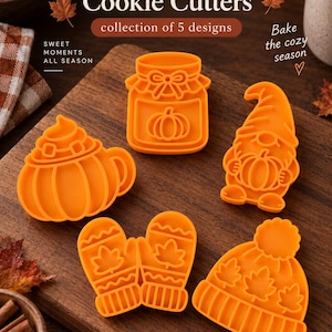 Peut inclure: Un ensemble de cinq emporte-pièces en plastique orange avec des motifs sur le thème de l'automne, incluant un bocal à citrouille, un gnome tenant une citrouille, une tasse avec de la crème fouettée, une paire de moufles et un bonnet à pompon.
