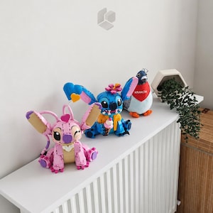 May include: A pink buildable character figure with large ears and a heart, a blue buildable character figure holding an ice cream cone, and a plush pigeon wearing a red scarf with the text KRAK&Oacute;W, all arranged on a white surface.
