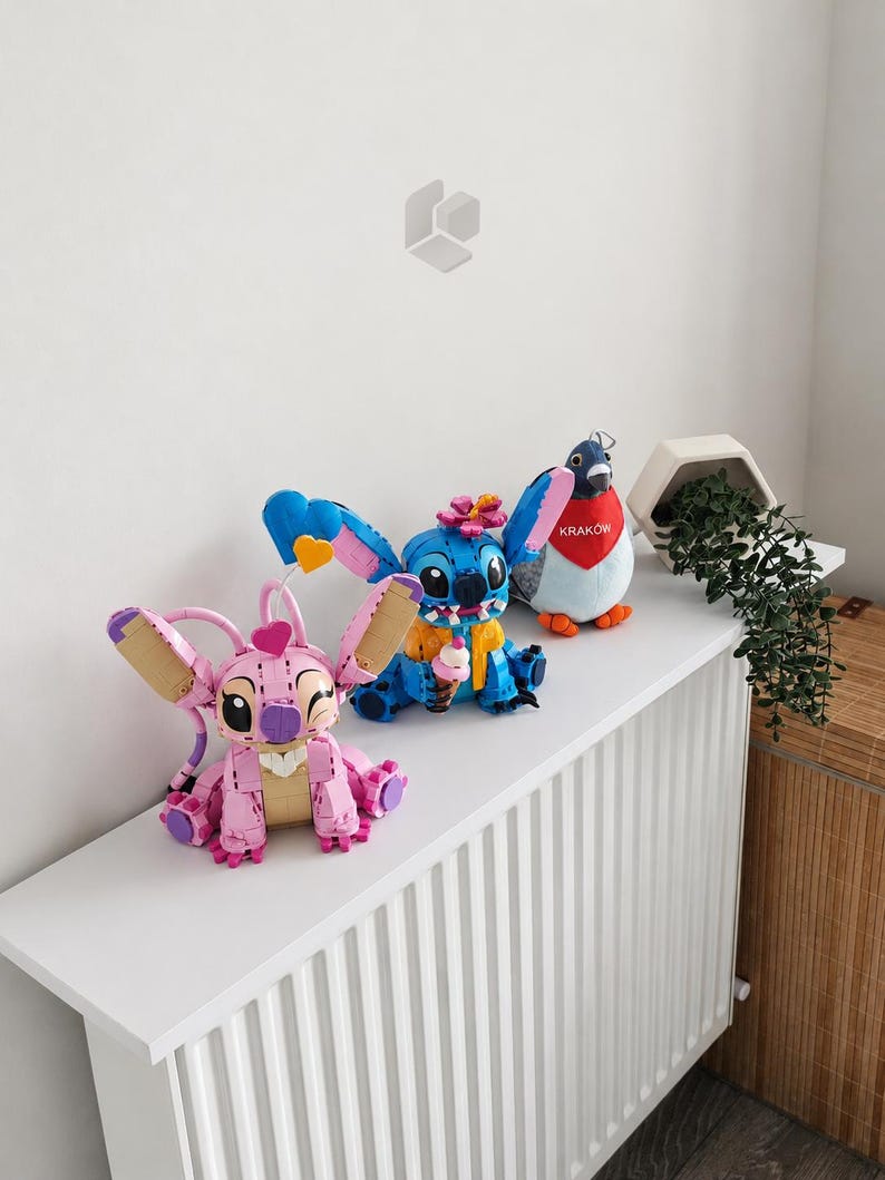 May include: A pink buildable character figure with large ears and a heart, a blue buildable character figure holding an ice cream cone, and a plush pigeon wearing a red scarf with the text KRAK&Oacute;W, all arranged on a white surface.