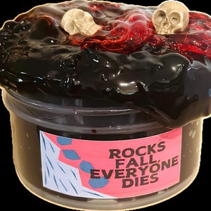 May include: A clear plastic container filled with black slime, topped with red gel and two small skull figurines. The container has a pink label with the text "ROCKS FALL EVERYONE DIES" and a mountain graphic.