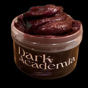 May include: A jar of dark purple slime with a shimmering, glittery texture. The container has a clear plastic body and a dark brown label with the words "Dark Academia" in white script.