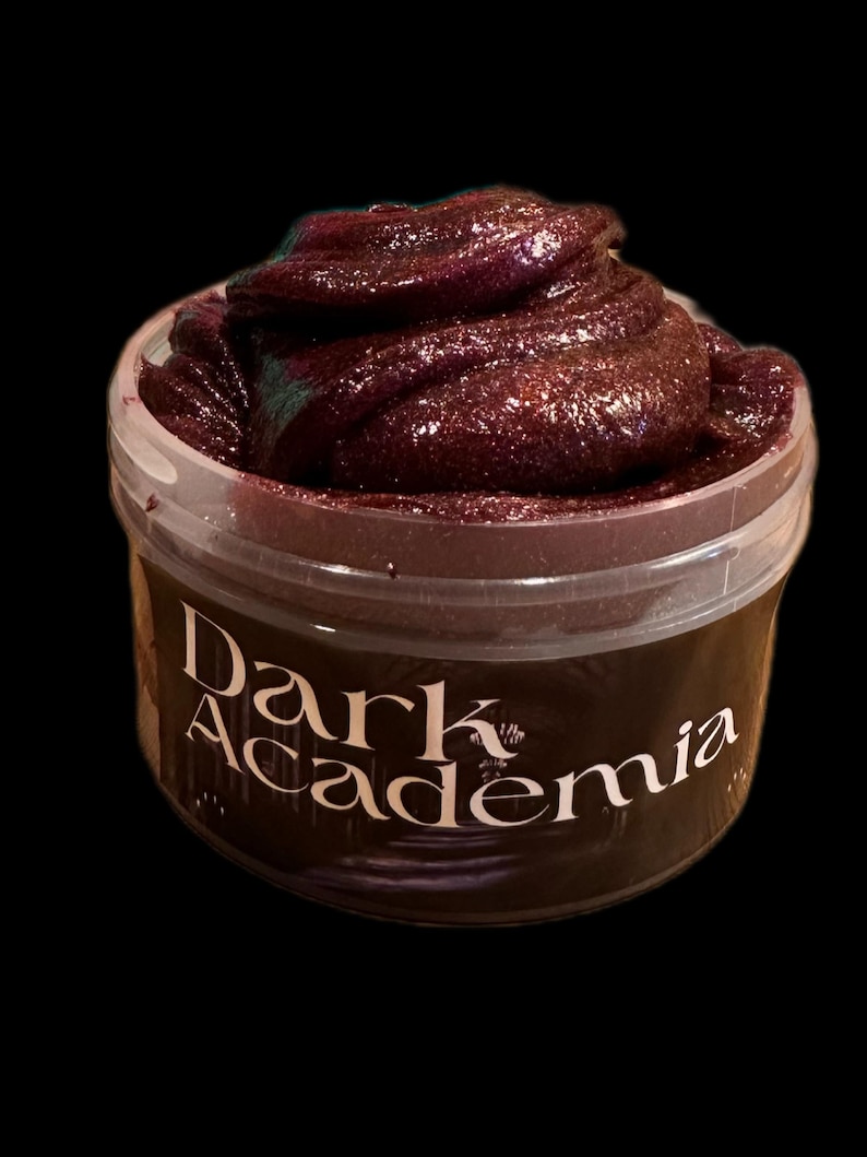 May include: A jar of dark purple slime with a shimmering, glittery texture. The container has a clear plastic body and a dark brown label with the words "Dark Academia" in white script.
