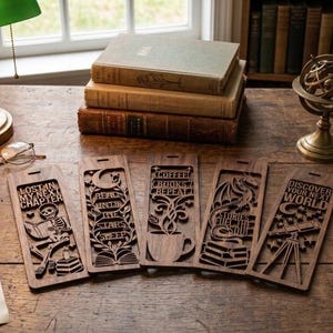 Op de afbeelding: Vijf rechthoekige bladwijzers van donker hout met gedetailleerde lasergesneden ontwerpen. De ontwerpen tonen een lezend skelet, maan en sterren, een dampende koffiekop, een draak met boeken en een telescoop met de tekst Discover Your Next World.