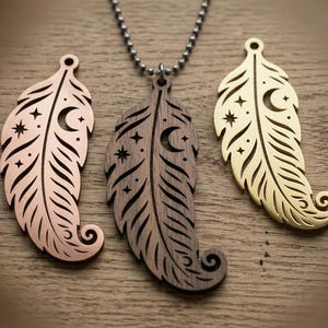 May include: Three feather-shaped pendants featuring cut-out celestial designs of stars and a crescent moon. One pendant is made of dark wood and hangs from a beaded chain, while the other two are metallic, one rose gold and one gold-toned.