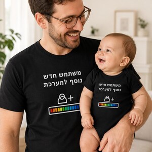May include: A black short-sleeved t-shirt and a matching black baby bodysuit. Both garments feature white Hebrew text that translates to 'New user added to the system', accompanied by a white user icon with a plus sign and a colorful loading bar graphic.